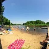 Ludzie odpoczywają i kąpią się nad **jeziorem Kozienickim** w słoneczny dzień.