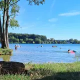 Słoneczny dzień nad jeziorem Pławniowice. Ludzie kąpią się i relaksują na dmuchanych zabawkach.