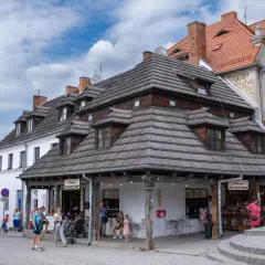 Tętniący życiem rynek w Kazimierzu Dolnym. Ludzie spacerują, kupują lody i gofry pod charakterystycznymi drewnianymi dachami.