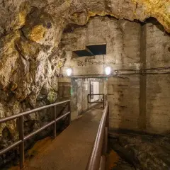Tunel w podziemiach Walimia, z metalową kładką i poręczą, prowadzi do oświetlonego przejścia. Odkryj te niezwykłe walim atrakcje.
