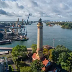 Latarnia morska góruje nad portem Świnoujście, gdzie widać dźwigi, statki i składy węgla.