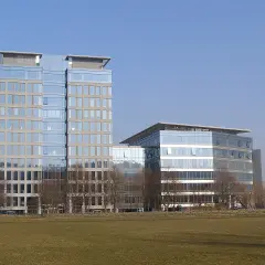 Nowoczesne budynki Olivia Tower i sąsiedni biurowiec z przeszklonymi fasadami, na tle błękitnego nieba.