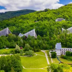 Nowoczesne budynki architektoniczne wkomponowane w zielone zbocza Beskidu Śląskiego. Uzdrowisko w Beskidzie Śląskim otoczone bujną roślinnością.