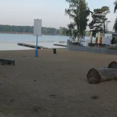 Plaża nad jeziorem Wonieść z pomostami, budynkiem kąpieliska i leżakami.