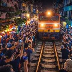 Pociąg przejeżdża wąską uliczką w Hanoi, otoczony tłumem ludzi z telefonami.