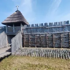 Drewniany gród obronny z wieżą i strzechą, pod niebieskim niebem.