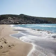 Piaszczysta plaża z falami i skalistym wzgórzem w tle.