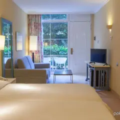 Pokój rodzinny w hotelu IFA Altamarena: łóżko, sofa, TV i wyjście na taras z widokiem na zieleń.
