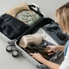 Kobieta pakuje do walizki: czarną kurtkę, zielony komplet, beżową torebkę, czapkę, buty, okulary i perfumy. Gotowa na podróż z enter air bagaż.