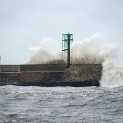 Potężne fale rozbijają się o kamienny falochron z latarnią morską.