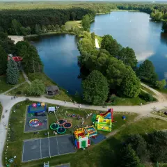 Rekreacja nad jeziorem w Bełchatowie: plac zabaw z dmuchańcami, trampolinami i zjeżdżalnią wodną, otoczony lasem i wodą.