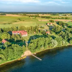Widok z lotu ptaka na domki letniskowe nad jeziorem w Mikołajkach, z pomostem i żółtymi kajakami.
