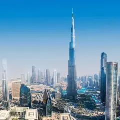 Widok z lotu ptaka na Dubaj, z dominującym Burdż Chalifa. Nowoczesne drapacze chmur i błękitne wody tworzą futurystyczny krajobraz.
