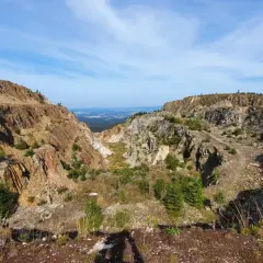 Krajobraz po wydobyciu kwarcu w kopalni Stanisław. Skarpy skalne, zarośla i niebo.