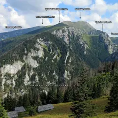 Widok na Tatry z Doliną Kościeliską. W oddali majaczą szczyty, a na pierwszym planie widać polanę z kilkoma drewnianymi halami stołami.