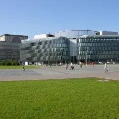 Plac Piłsudskiego w Warszawie. Nowoczesny budynek z przeszkloną fasadą obok klasycystycznego gmachu.