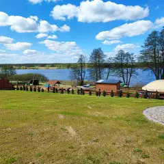 Piękny dzień nad jeziorem skarlińskim. Błękitne niebo z białymi chmurami, zielona trawa i spokojna tafla wody.