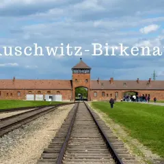 Brama obozowa Auschwitz-Birkenau z wieżą i torami kolejowymi.