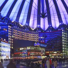 Nocny widok na Sony Center w Berlinie, z oświetlonym dachem i fasadami budynków, pełen ludzi spacerujących po placu.