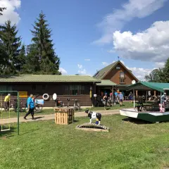 Na placu przed drewnianymi budynkami, wśród drzew, stoi łódź i krowa na moście. Je je jeleń witnica, jakby czekał na wycieczkę.