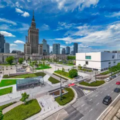 Warszawski plac defilad z Pałacem Kultury i Nauki, nowoczesnym budynkiem i ruchliwą ulicą.