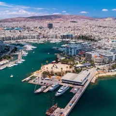 Widok z lotu ptaka na tętniący życiem piraeus port z licznymi jachtami i statkami, otoczony zabudowaniami i górami w tle.