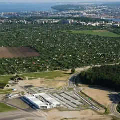 Widok na lotnisko Kosakowo z nowymi budynkami i drogami, w tle rozległe ogródki działkowe i panorama Gdyni.