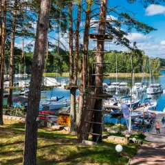 Linowy park rozrywki w lesie nad jeziorem z przystanią pełną jachtów.