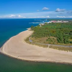 Piękny widok na piaszczystą plażę i turkusowe morze w Helu. W oddali widać miasteczko i las.
