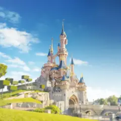 Zamek w Disneylandzie Paryż na tle błękitnego nieba z chmurami i zielonymi drzewami.