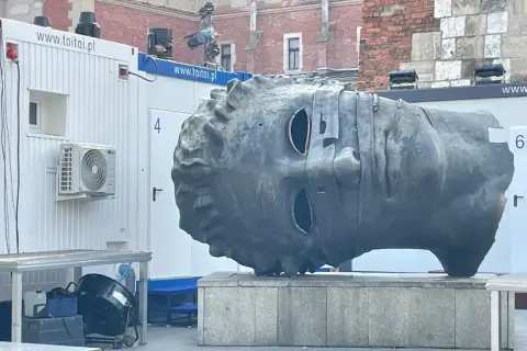 Monumentalna głowa na rynku w Krakowie, z pustymi oczodołami, wygląda jakby patrzyła w dal.