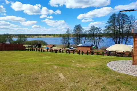 Piękny dzień nad jeziorem skarlińskim. Błękitne niebo z białymi chmurami, zielona trawa i spokojna tafla wody.