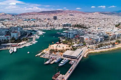 Widok z lotu ptaka na tętniący życiem piraeus port z licznymi jachtami i statkami, otoczony zabudowaniami i górami w tle.