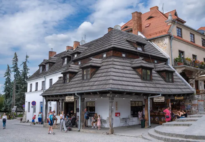 Tętniący życiem rynek w Kazimierzu Dolnym. Ludzie spacerują, kupują lody i gofry pod charakterystycznymi drewnianymi dachami.