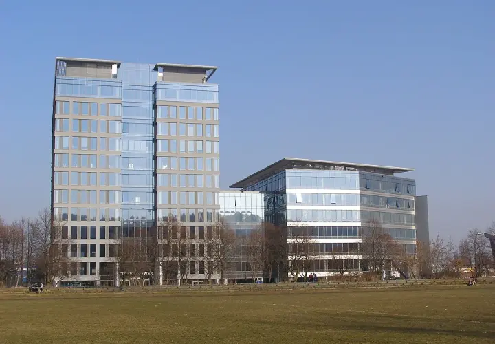 Nowoczesne budynki Olivia Tower i sąsiedni biurowiec z przeszklonymi fasadami, na tle błękitnego nieba.