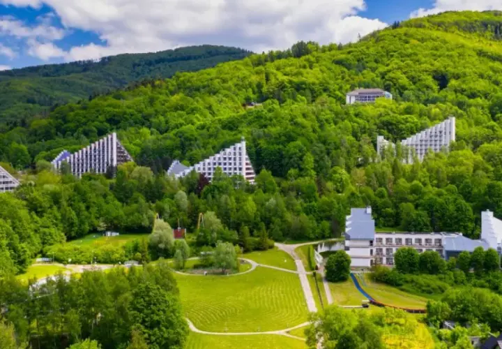 Nowoczesne budynki architektoniczne wkomponowane w zielone zbocza Beskidu Śląskiego. Uzdrowisko w Beskidzie Śląskim otoczone bujną roślinnością.