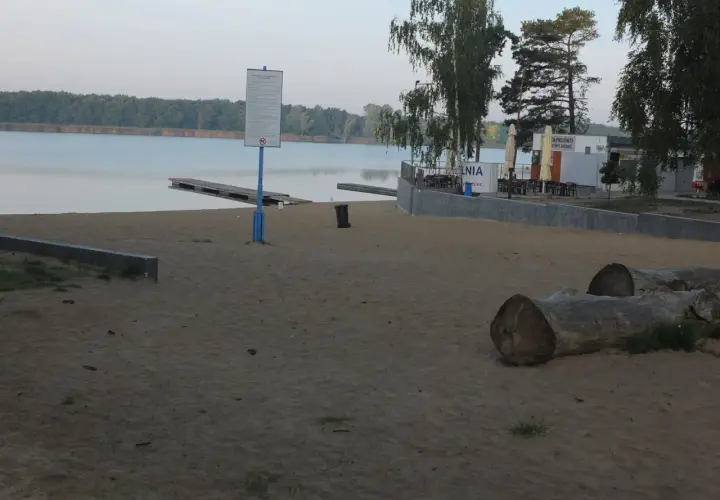 Plaża nad jeziorem Wonieść z pomostami, budynkiem kąpieliska i leżakami.