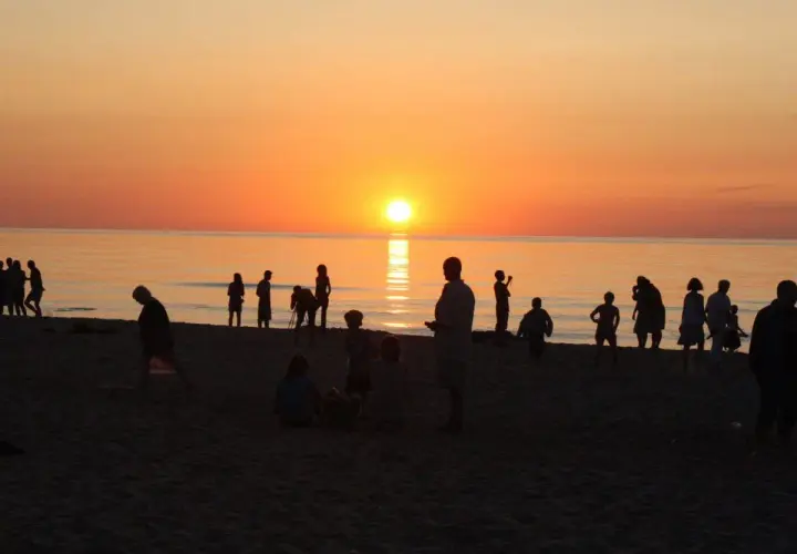 Sylwetki ludzi na plaży o zachodzie słońca nad morzem.
