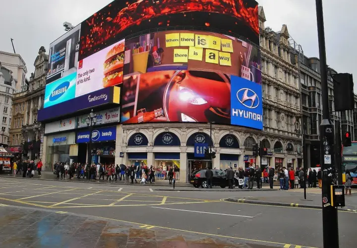 Tętniący życiem Piccadilly Circus w Londynie z neonowymi reklamami, w tym Samsung, McDonald's i Hyundai. Tłum ludzi na chodniku.