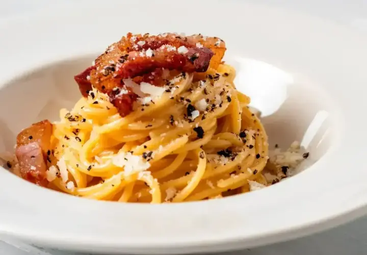 Pyszne spaghetti carbonara z chrupiącym guanciale, posypane parmezanem i czarnym pieprzem.