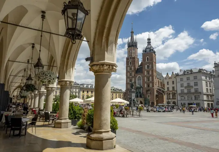 Urokliwe arkady Sukiennic w Krakowie, z widokiem na Kościół Mariacki. Stare miasto w Krakowie tętni życiem.