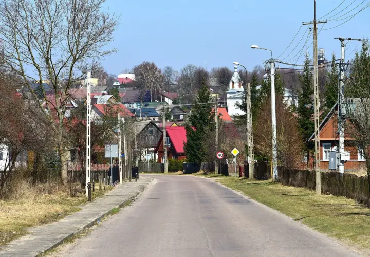 Droga prowadzi do malowniczej wsi Krynki. W oddali widać kolorowe dachy domów i kościół, tworząc urokliwe krynki atrakcje.