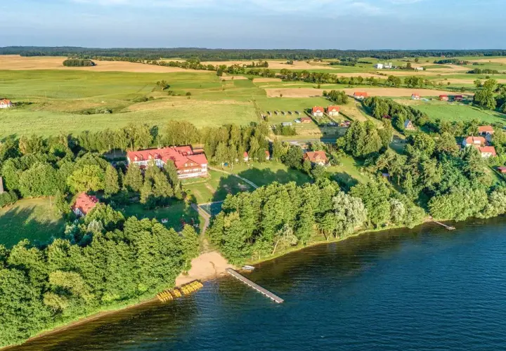 Widok z lotu ptaka na domki letniskowe nad jeziorem w Mikołajkach, z pomostem i żółtymi kajakami.