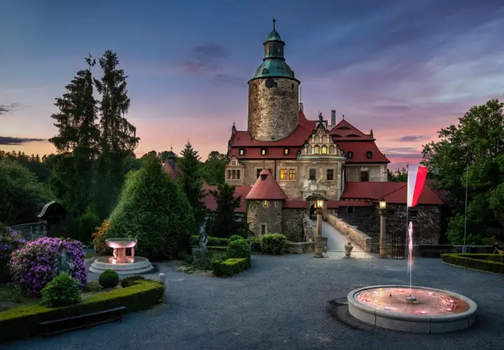 Zamek Czocha o zmierzchu, z fontannami i kwitnącymi rododendronami. Odkryj atrakcje w okolicy tego malowniczego miejsca.