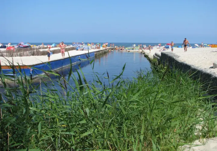 Słoneczny dzień nad kanałem w Karwi. Ludzie odpoczywają na plaży, a woda przyciąga do kąpieli. To jedna z wielu atrakcji w okolicy.