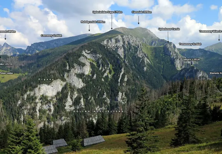 Widok na Tatry z Doliną Kościeliską. W oddali majaczą szczyty, a na pierwszym planie widać polanę z kilkoma drewnianymi halami stołami.