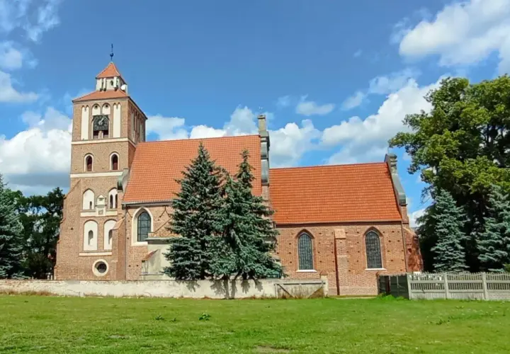 Nieszawa atrakcje: ceglany kościół z wieżą i zegarem, otoczony zielenią, na tle błękitnego nieba z chmurami.
