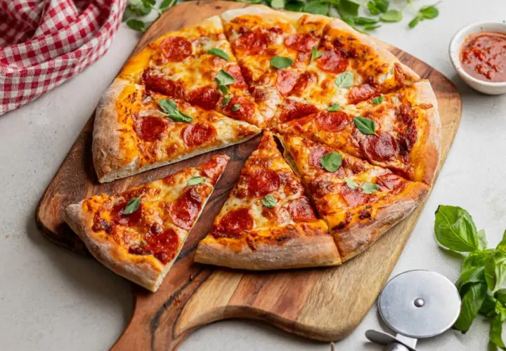 Krojona pizza pepperoni z serem i bazylią na drewnianej desce.
