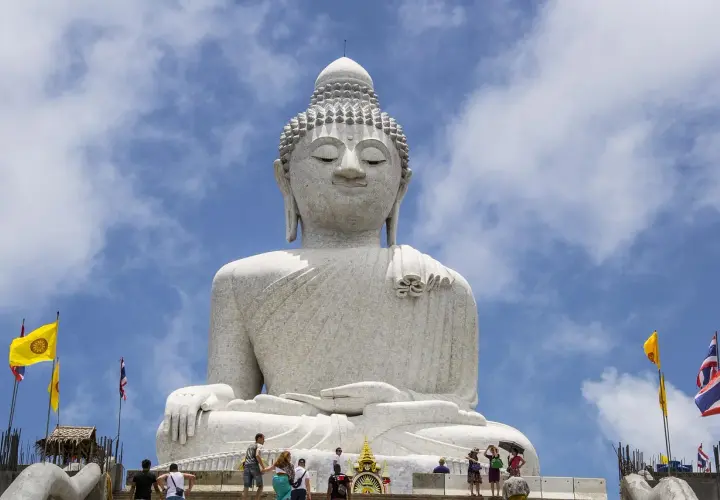 Wielki Budda na Phuket, majestatyczna biała statua na tle błękitnego nieba z chmurami. Turyści wchodzą po schodach.