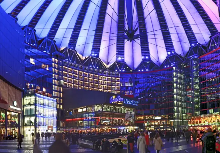 Nocny widok na Sony Center w Berlinie, z oświetlonym dachem i fasadami budynków, pełen ludzi spacerujących po placu.